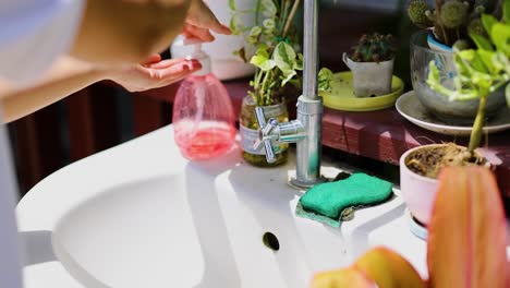 a person washes hands at an outdoor sink surrounded by plants in bright sunlight, emphasizing cleanliness and nature