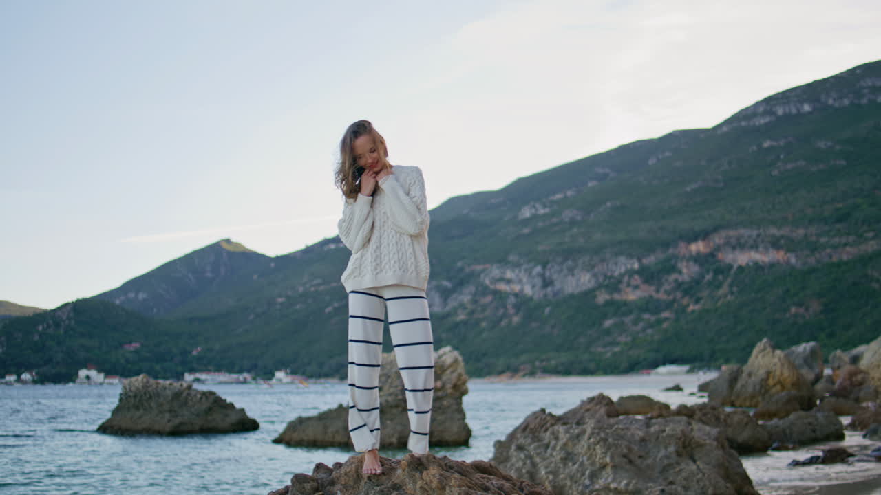 Tourist posing windy beach. Happy woman standing on rocks ocean shore barefoot