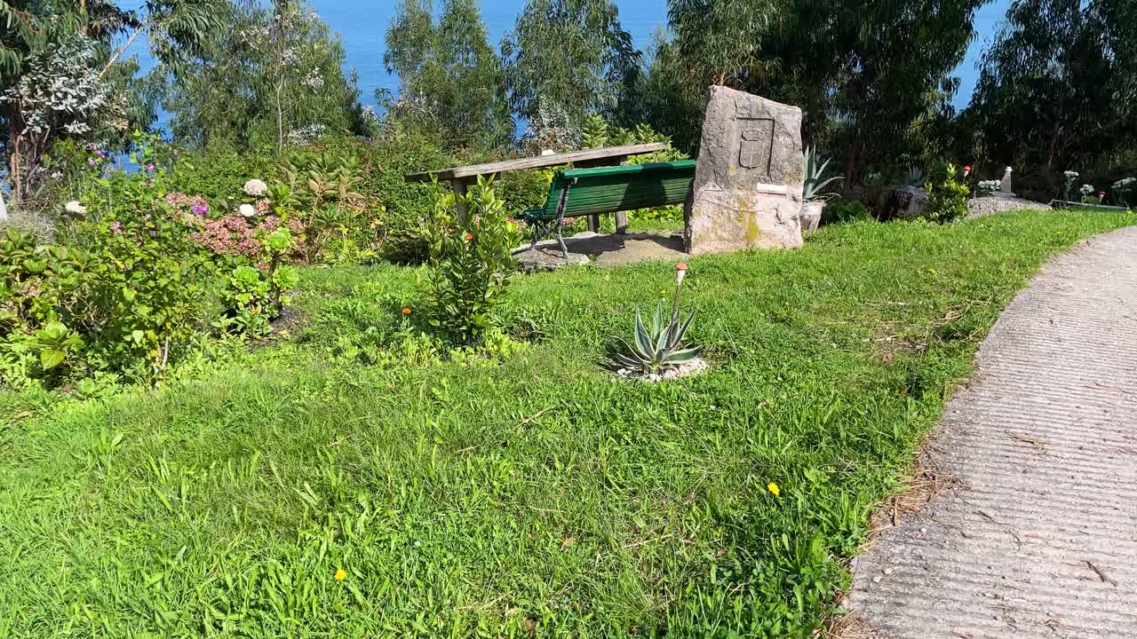 filming of a small public park located in an enclave with privileged views of the sea, it consists of a wooden bench, a table, decorative plants around it and a stone with a shield