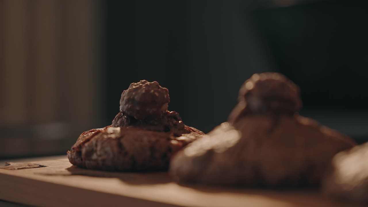 Mano che posiziona con cura un morbido biscotto al cioccolato con guarnizione dolce su un vassoio di legno.