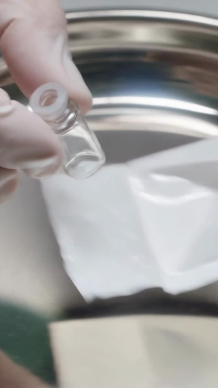 Video verticale: Apertura di un blister, mani guantate che sollevano una fiala su un vassoio di metallo, preparazione per il laboratorio.
