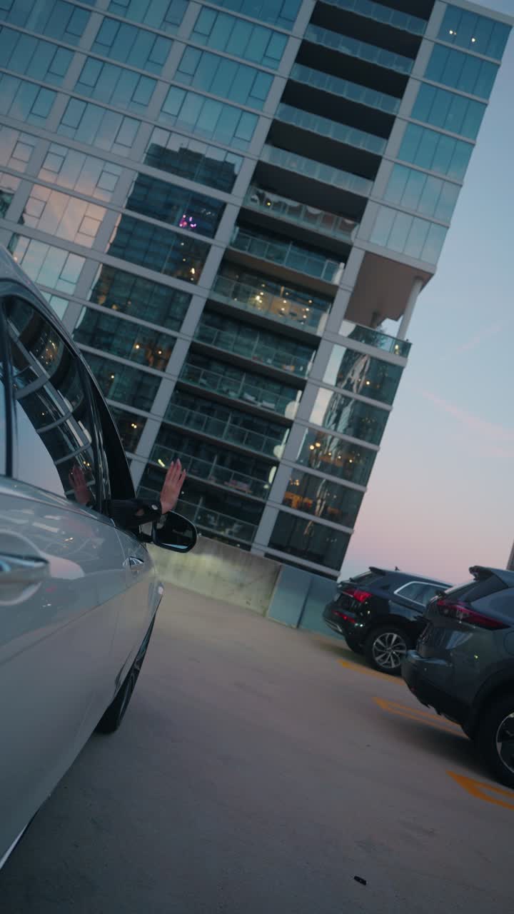 City moment as a woman's hand rests out the car window on a rooftop garage with skyline views at sunset.