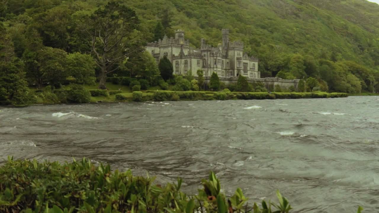 Kylemore Abbey nestled between forested hills and a serene lake in Connemara, Ireland. Historic castle with gothic architecture surrounded by nature and misty mountains.