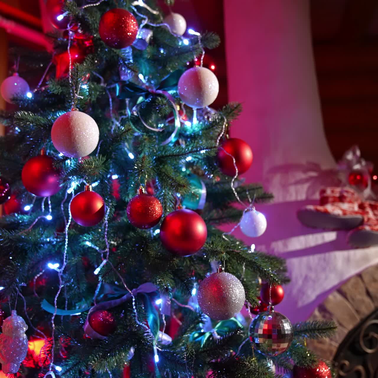 Beautiful Christmas tree with lights and ribbons. Amazing fir tree decorated with Christmas balls near the cozy fireplace in the living-room