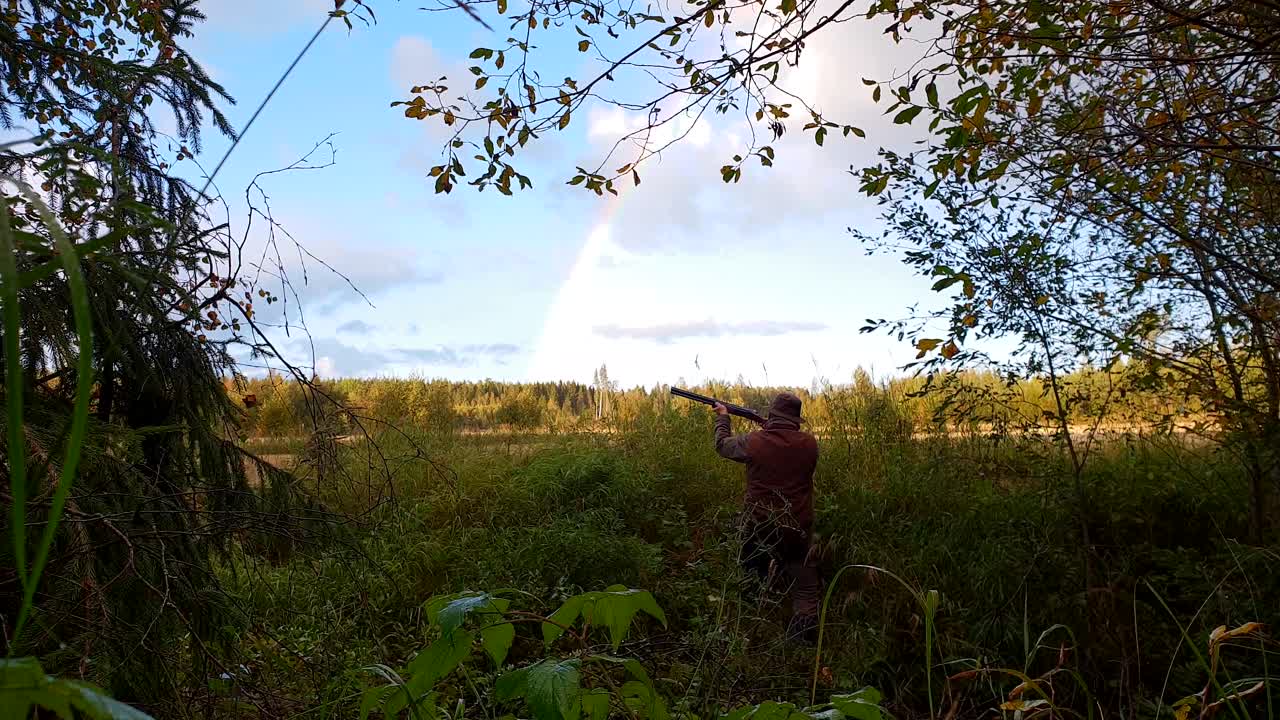 Bellissimo arcobaleno e cacciatore di uccelli che punta il fucile in uno splendido scenario naturale