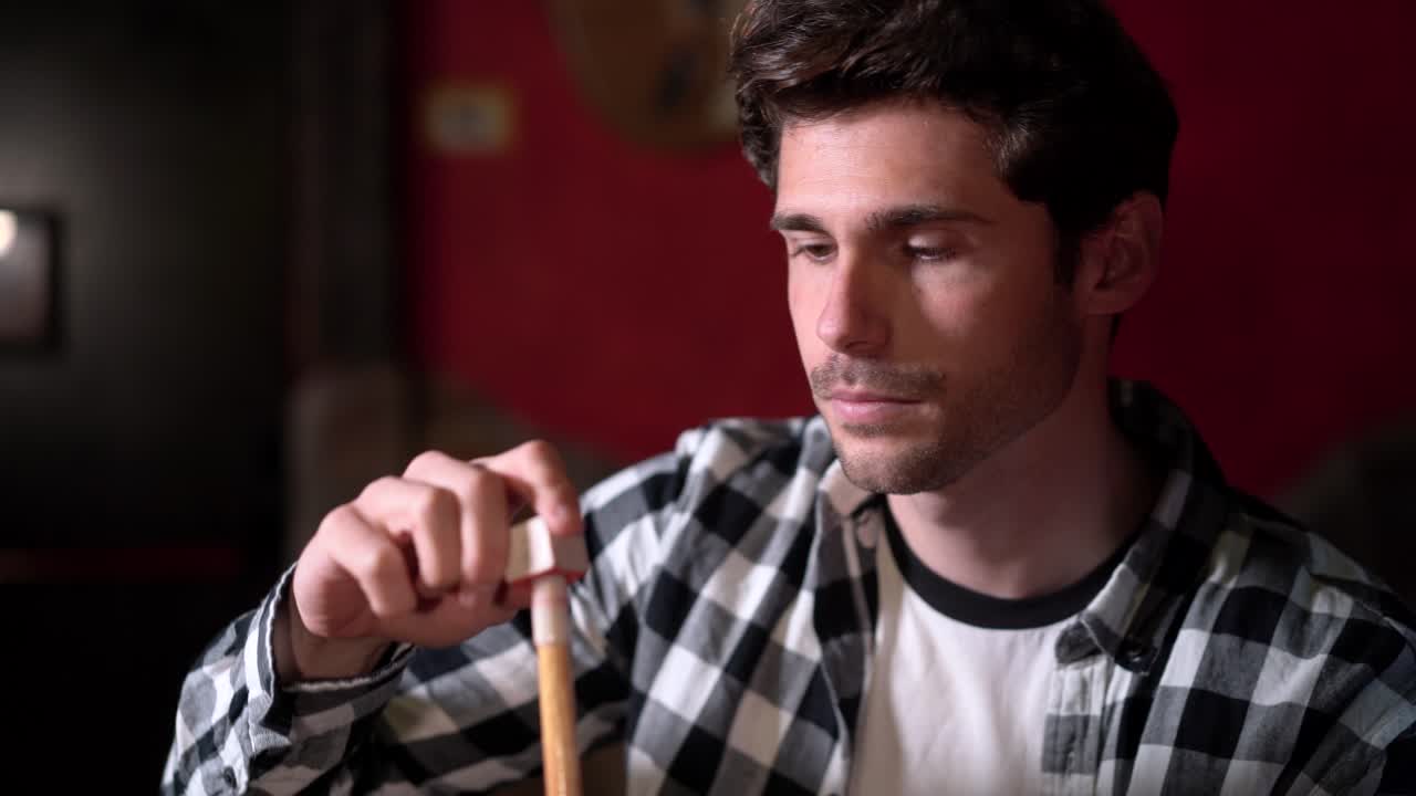 Focused man chalking pool cue before game