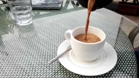 tea or indian masala chai being poured in a white cup on a cafe table