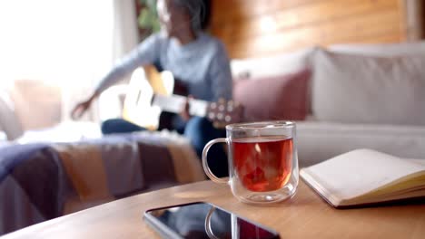 happy african american woman playing guitar using laptop in living room, in slow motion