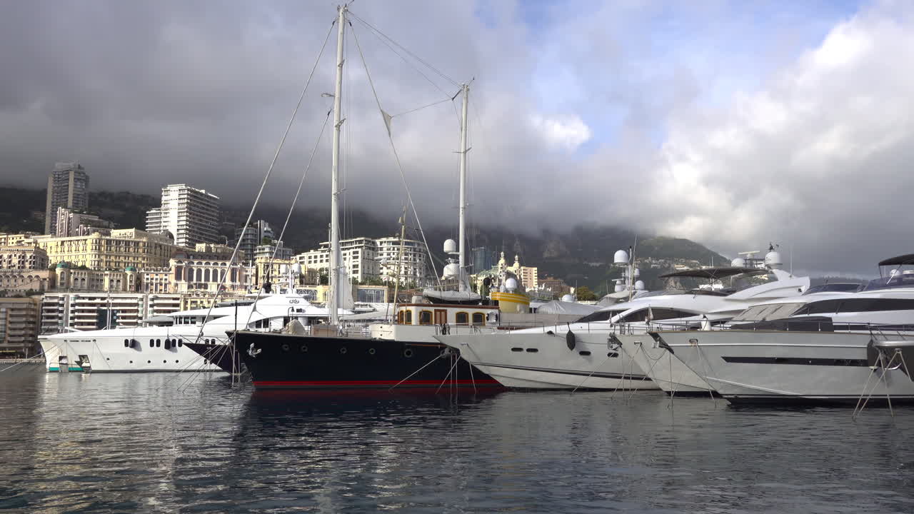 La Condamine, Monaco - July 4, 2025: Row of sleek luxury yachts, docked in Port Hercules with the Monaco cityscape and misty hills in the background