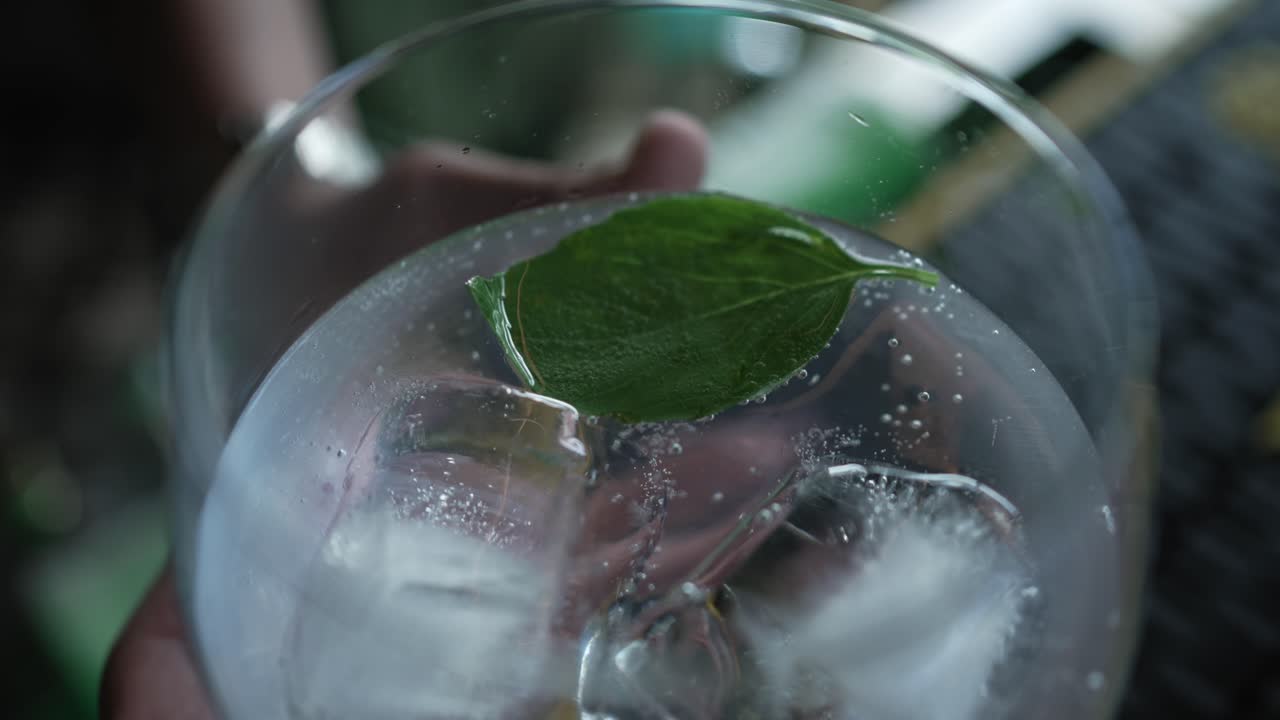 refreshing gin and tonic lifted by hand from bar with mint and ice