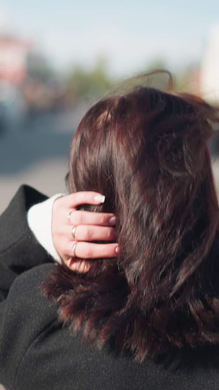 은 도시 거리에서 왼손에 세 개의 반지를 보여주는 검은 코트를 입은 갈색 머리카락을 가진 여자의 근접 뒷면