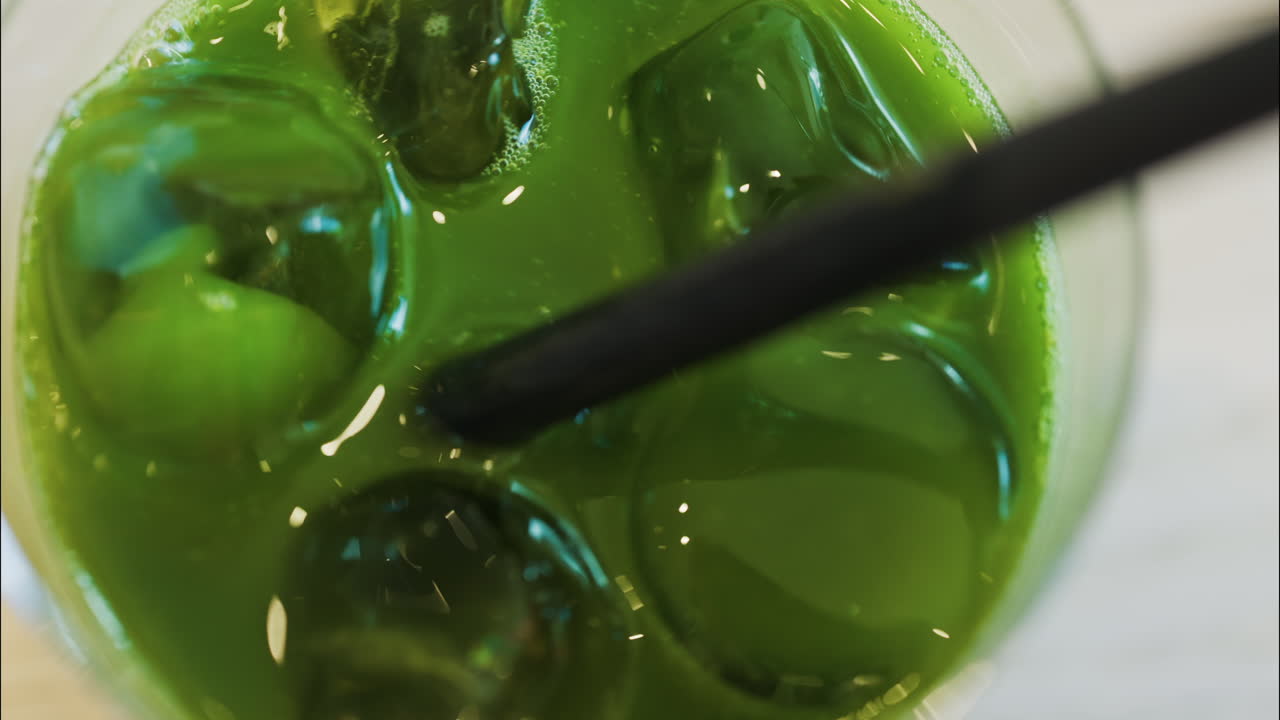 Close up of a hand mixing an iced matcha in a glass with a black straw at a cafe