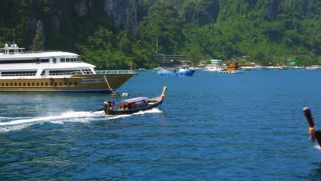 A-Boat-Traveling-On-The-Ocean,-Passing-By-Different-Sea-Vessels-While-Approaching-A-Breathtaking-Lush-Green-Island-On-Sunny-Day---Wide-Shot