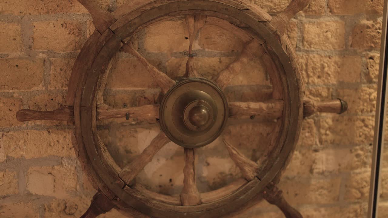 Antique wooden ship wheel slowly rotating on display, warm lighting, brick wall background, static camera