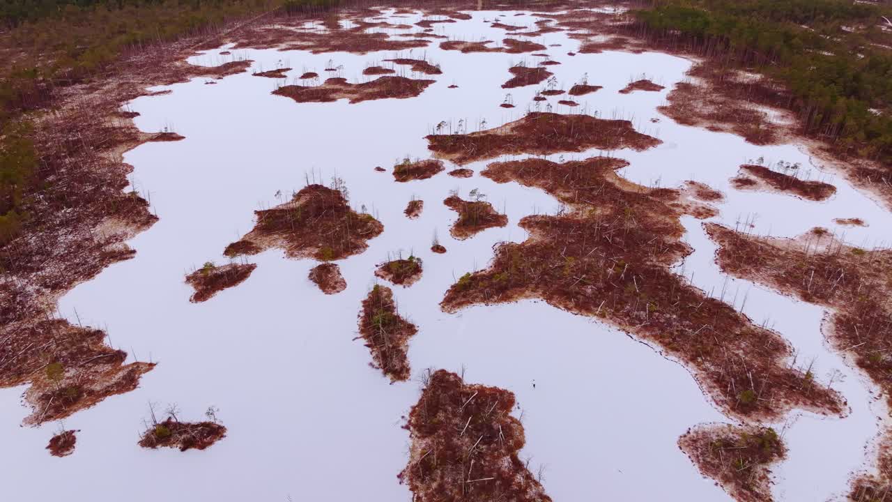 Top down aerial of icy bog lake with islands and solo skater at winter sunrise