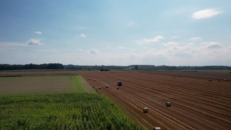 aerial - rural atmosphere with natural landscape - view of a mowed field of crops and working agricultural machinery in the field