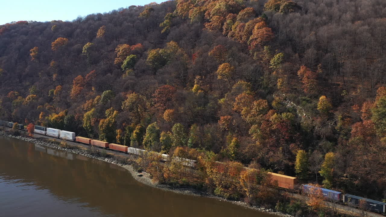 An aerial view on the south side of the Mid-Hudson Bridge. The camera dollys in, descends to Highland Landing on the west bank of the Hudson River. There is a long cargo train - It's a sunny day.