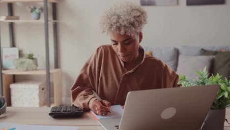 african woman calculates domestic bills pay loan payments online on laptop