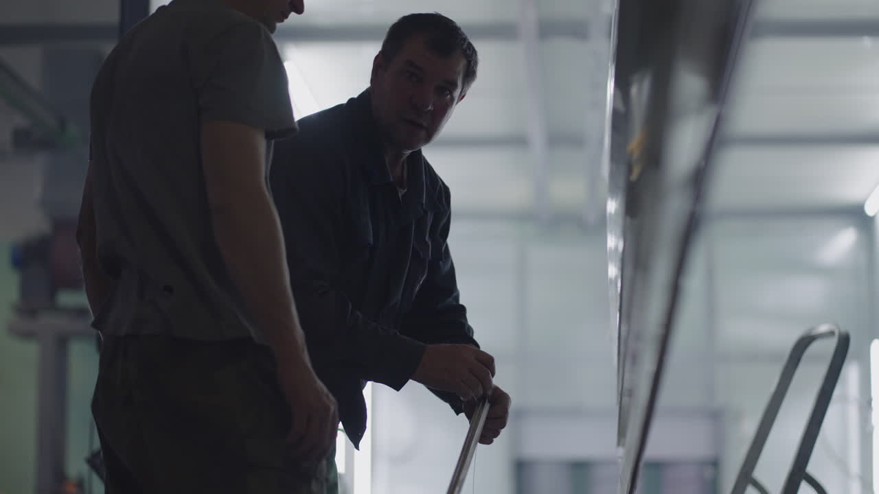 dos pintores masculinos preparan elementos metálicos de acero para pintar fijándolos en suspensiones. pintar piezas en la sala de producción. filmar en cámara lenta.