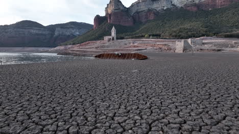 shipwreck of boat on dry shores of sau marsh with church ruin in background, catalonia, spain