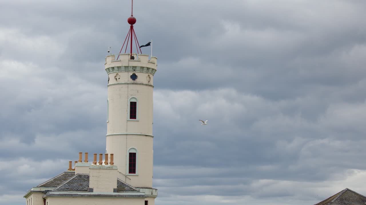 Static shot of lighthouse tower under overcast sky, subtle bird movement, natural daylight, no motion