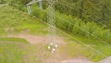 aerial view of a worker climbing down a transmission tower amidst forest