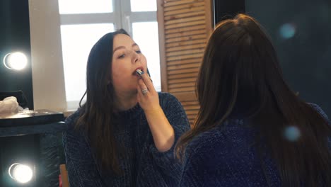 mujer aplicando lápiz labial frente a un espejo