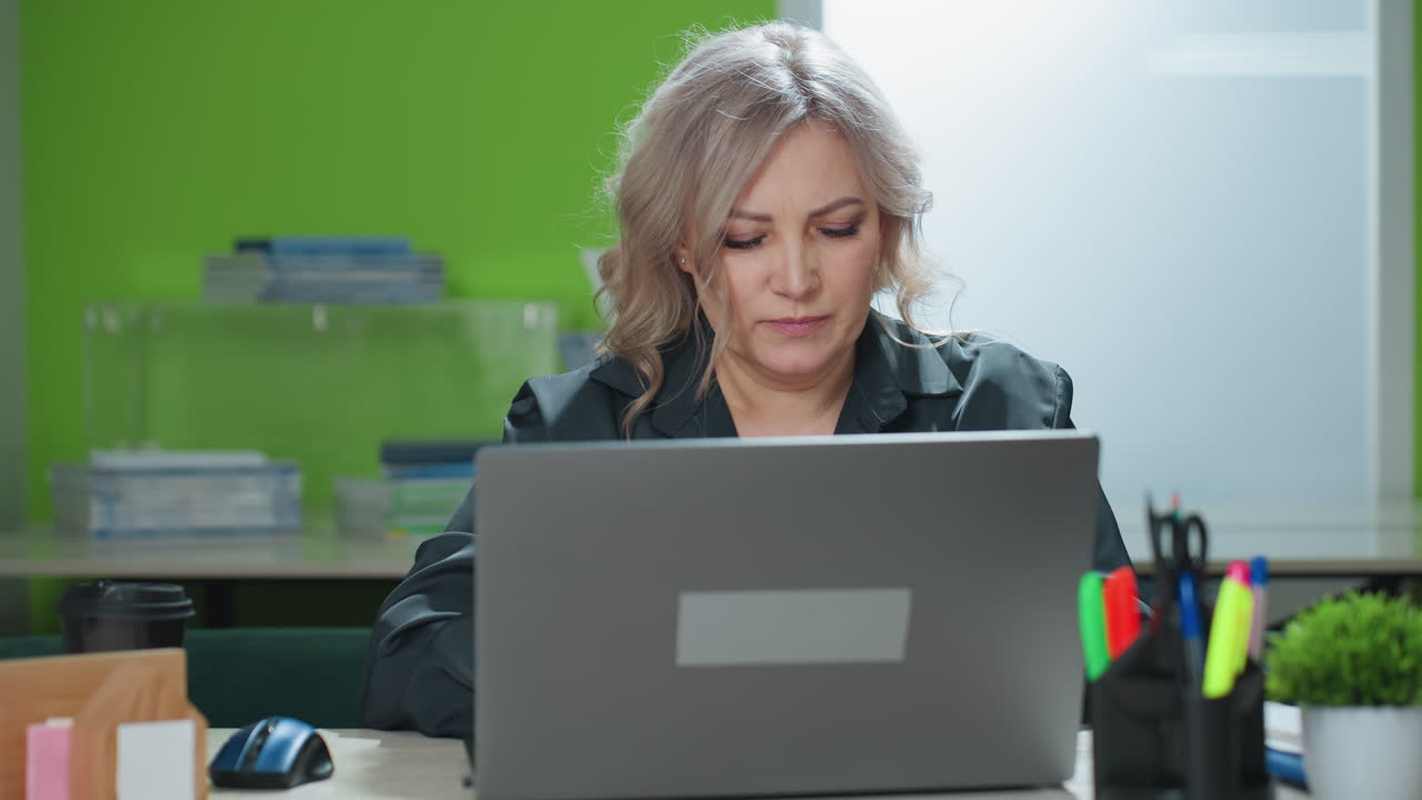 Professional real estate agent engaged in phone conversation with client while interacting with laptop in bright modern office setting, focused on multitasking and discussing property details