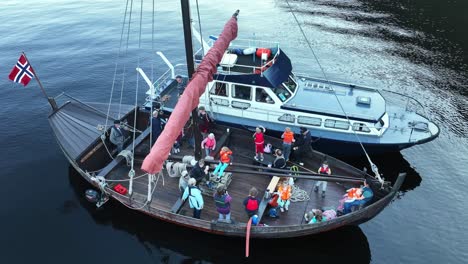drone orbits a historic wooden ship moored with a modern support vessel, filled with children and adults on deck exploring the fjord
