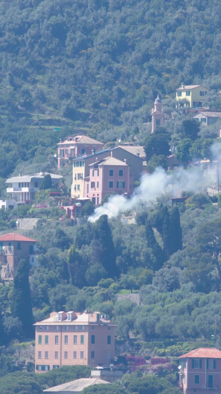 Campo lungo statico di fumo bianco che si diffonde attraverso un villaggio mediterraneo in collina con case colorate