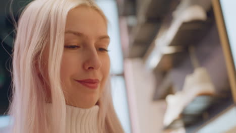 closeup on poised fashion lover with platinum hair smiling while lifting item inside modern store, eyes glitter under warm spotlights, expressing joy during shopping moment among displays