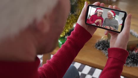 Hombre-Caucásico-Con-Sombrero-De-Santa-Usando-Un-Teléfono-Inteligente-Para-Una-Videollamada-Navideña-Con-Una-Familia-Sonriente-En-La-Pantalla