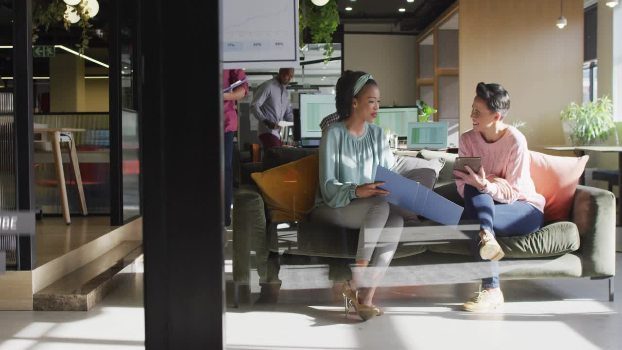 Two women sitting on couch using tablet for marketing, team passing, sparking alerts piling, fading