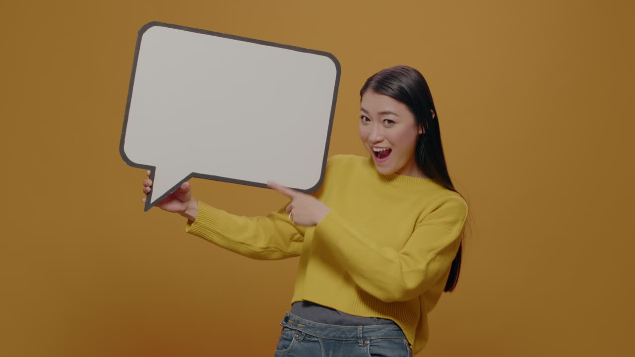 Cheerful woman pointing at empty speech bubble in studio