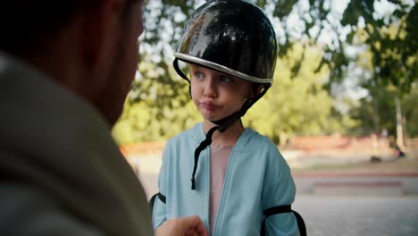 The-father-of-a-little-boy-in-a-blue-T-shirt-with-blue-eyes-helps-him-put-on-a-black-helmet-and-a-blue-jacket.-Little-boy-preparing-to-ride-a-skateboard-outdoor-activity