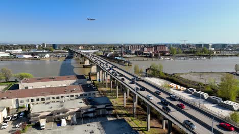 Avión-Volando-En-El-Cielo-Sobre-El-Río-Fraser-Con-Vehículos-En-El-Puente-De-La-Calle-Roble,-Autopista-99-En-Canadá