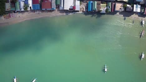 Aerial-view-of-El-Nido-town-backwards-tracking-to-emerald-green-waters-with-traditional-boats-in-Palawan,-the-Philippines