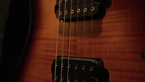 cluse up view of an electric guitar. detail of instrument along guitar wooden pickguard, fingerboard and golden strings to guitar neck. illuminated guitar in dark room highlighting the fine details