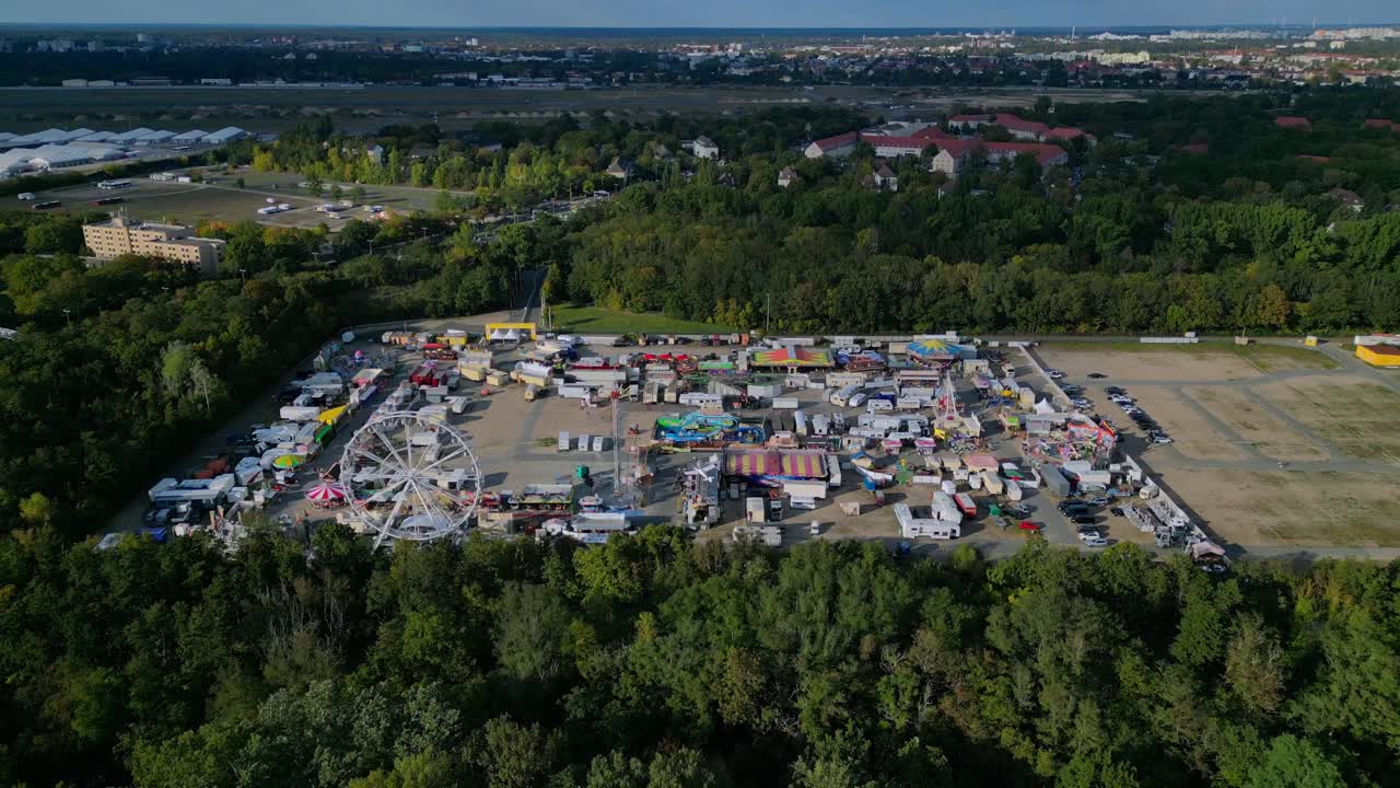 Berlin funfair showing a Ferris wheel, amusement rides, and various stalls from an aerial perspective. Majestic aerial view flight descending drone