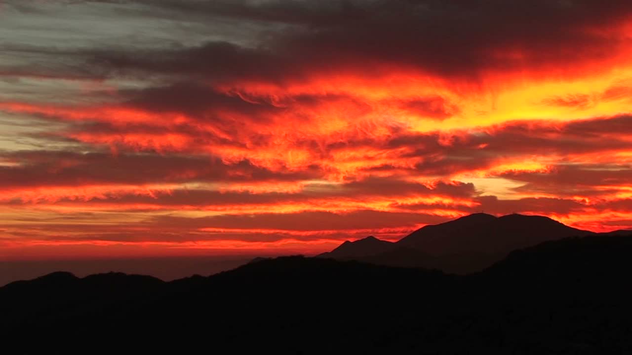 Inquadratura media di un arrampicatore in silhouette contro un tramonto infuocato in California