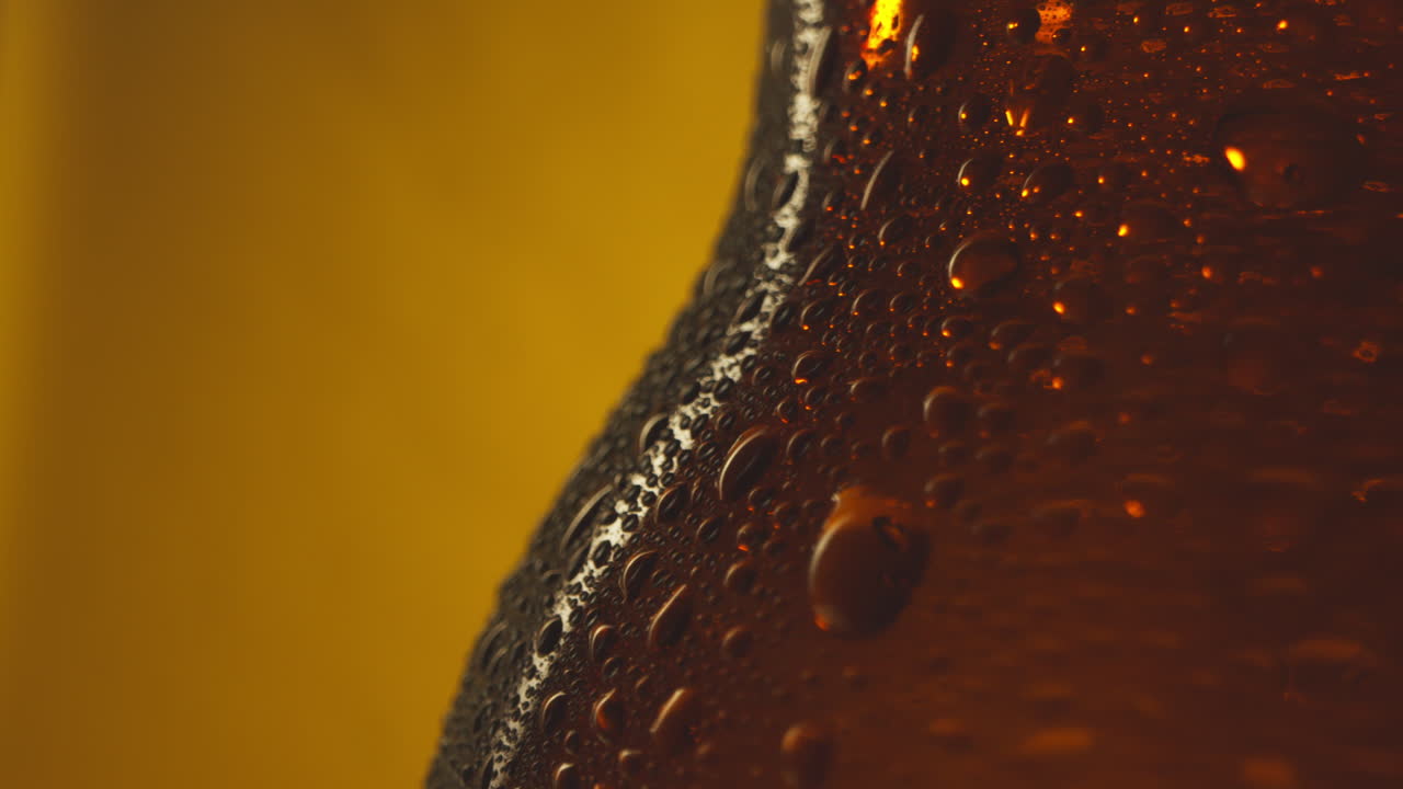 macro disparo de gotas de condensación en una botella giratoria de cerveza fría o bebidas gaseosas contra un fondo amarillo 1