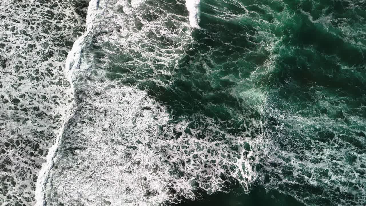 High aerial, slow motion view of powerful waves with white caps crashing on beautiful, scenic beach and colourful surfing boards