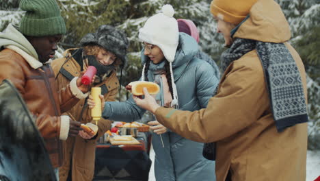 friends making hot dogs on winter picnic in forest