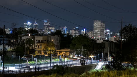 Lapso-De-Tiempo-De-Una-Parada-Del-Sistema-Ferroviario-Suburbano-Denver-Rtd-Por-La-Noche-Con-Los-Rascacielos-Del-Centro-A-Lo-Lejos