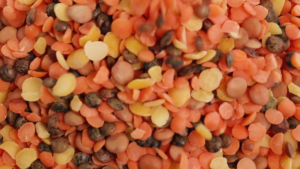 A vibrant mix of lentils and seeds cascades onto a surface, creating a colorful and textured display