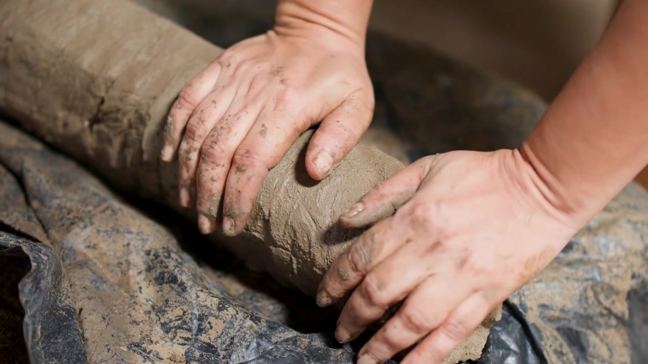 Close-up of a craftsman's hands kneading and modeling wet clay on a rotating wheel.