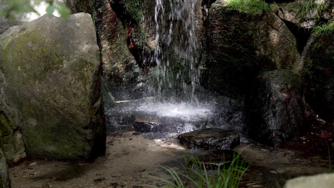 petite chute d'eau frappant le sol rocheux plat, éclaboussant sur le bord dans le jardin zen japonais