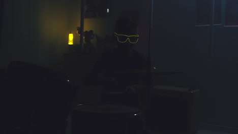 teenager playing drums during home concert zoom out view of teen musician in sunglasses playing drums under blue neon illumination and pretending to be rock star during home concert in bedroom