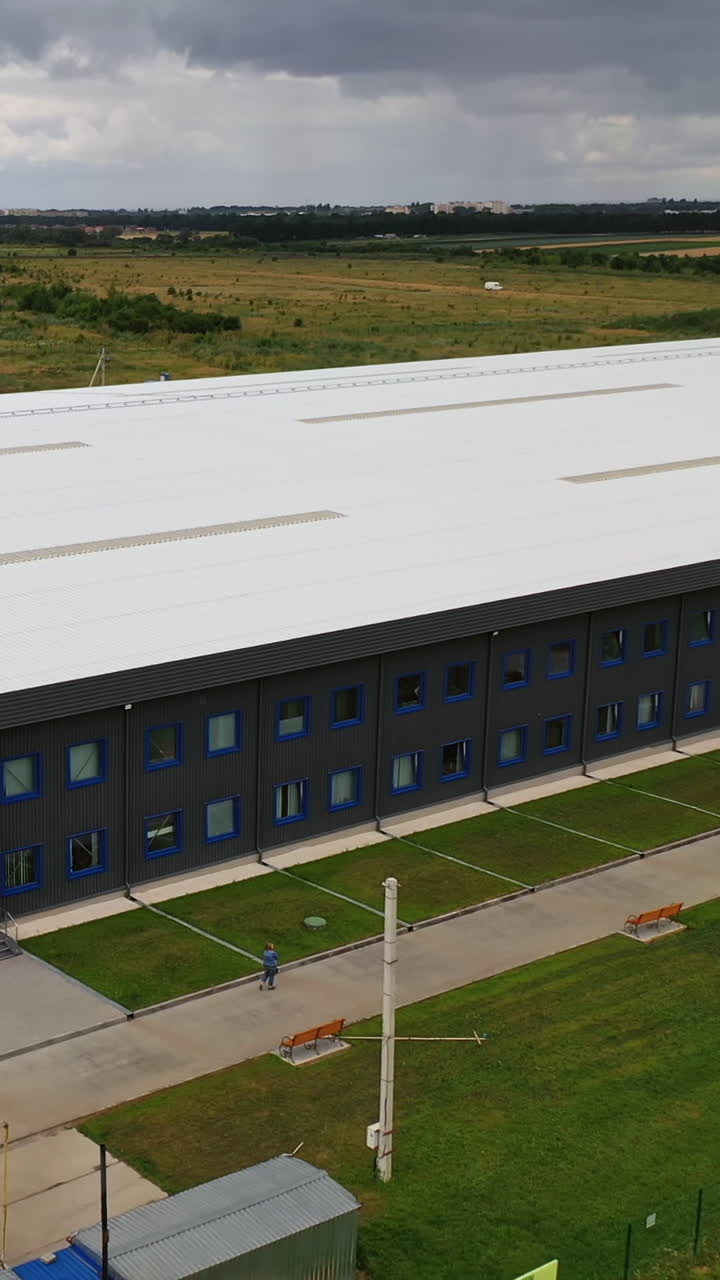 Modern industrial exterior. Large factory building among green fields. New building from outdoors. Aerial view. Vertical video