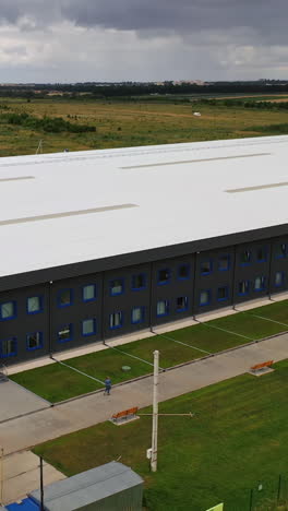 modern industrial exterior. large factory building among green fields. new building from outdoors. aerial view. vertical video